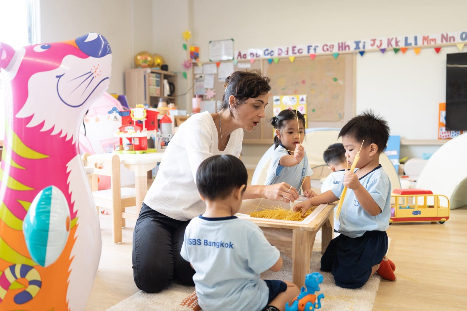 A teacher kneeling with Toddlers at the sensory table