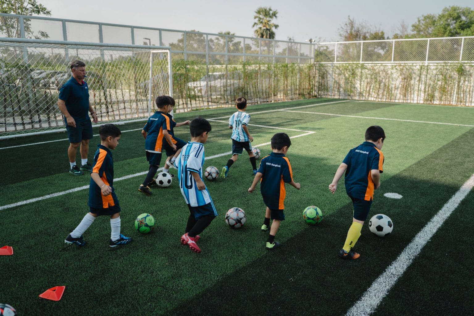 Primary pupils dribbling footballs on the pitch
