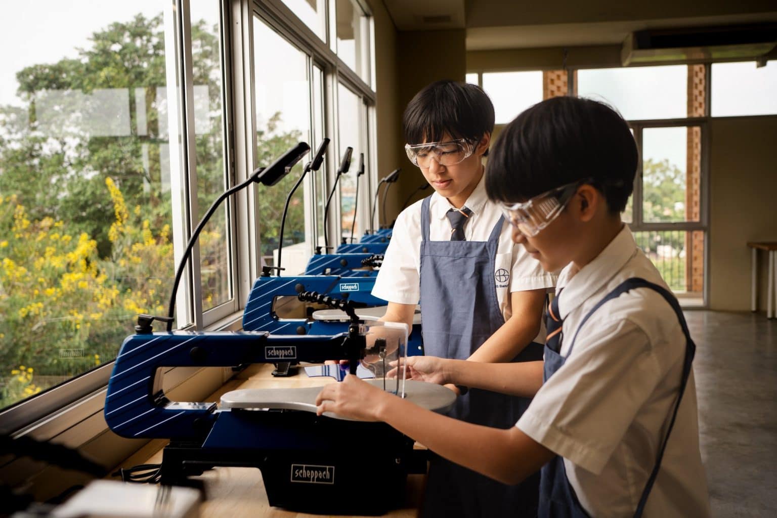 Two students cutting materials on the scroll saws in the Design Innovation workshop